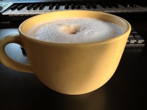 Kaffee mit aufgeschäumter Milch in großer, gelber Tasse.